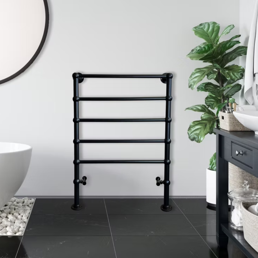 Lifestyle image of the Radox Edwardian 1000mm x 700mm Matt Black Floor Standing Heated Towel Rail mounted on a white bathroom wall, next to a freestanding bath